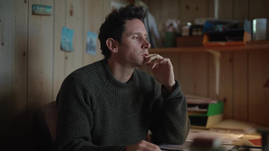 A man in an office thinking while holding a pen