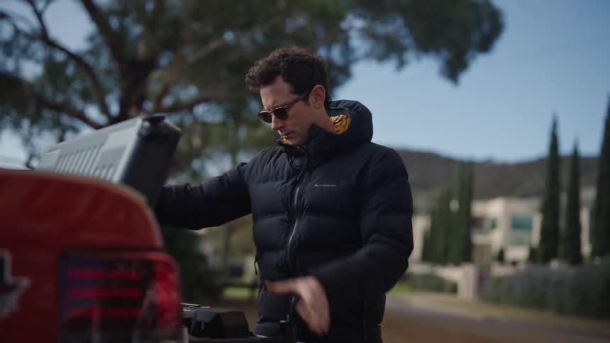 A man stands behind his truck and opens a black case