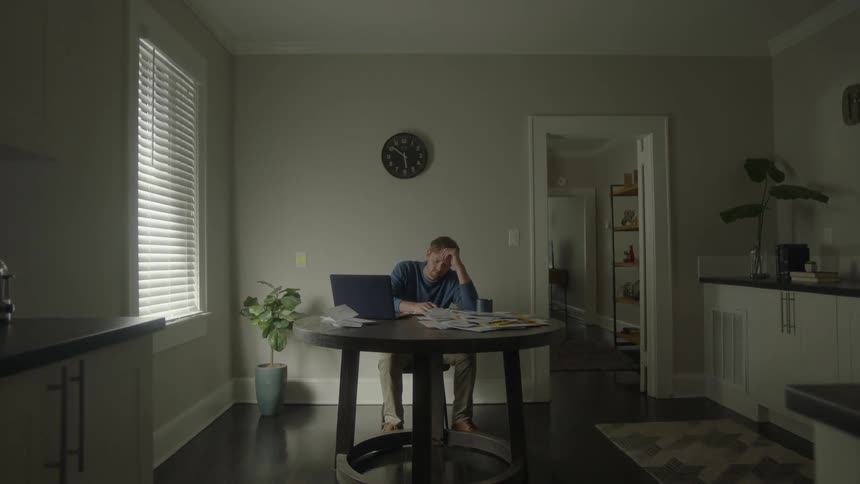 A man possibly working on a computer is tired and rests his head on his hand
