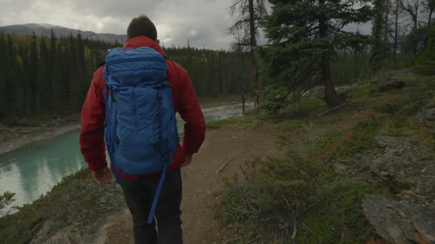 A man wearing a backpack while he hikes along cliffs that overlook a mountain river