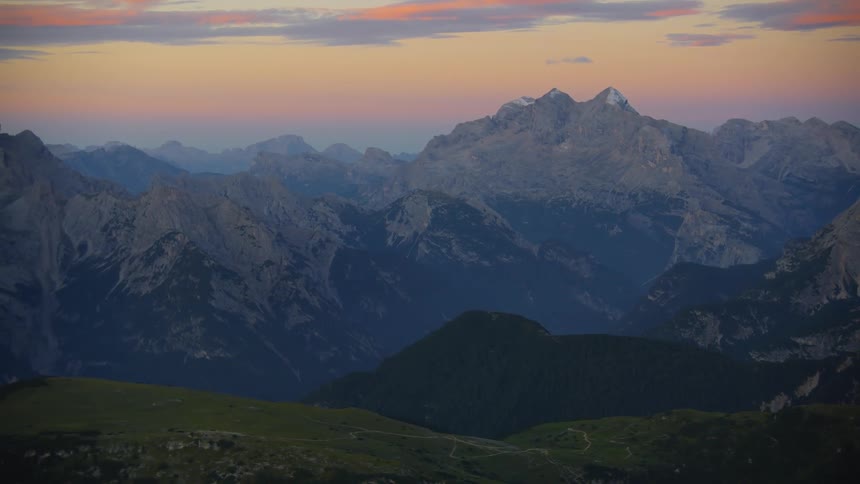 A view of a mountain range with peak formations and cliffs against a reddish sky