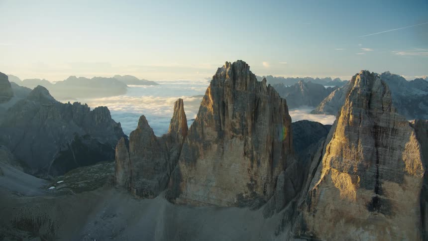 An aerial view of a mountain range and cliffs above the cloud level with sunlight reflections