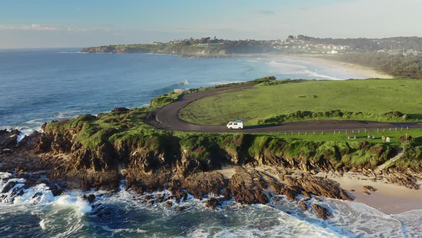 A small van passing along a road that runs close to the sea coast