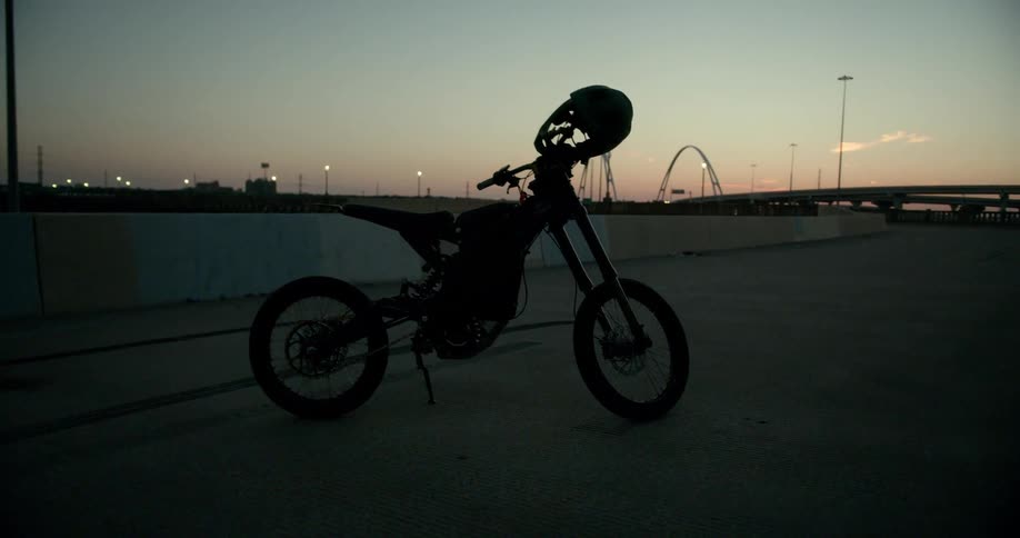 Cycle parked on pavement far from overpass is silhouetted against red horizon