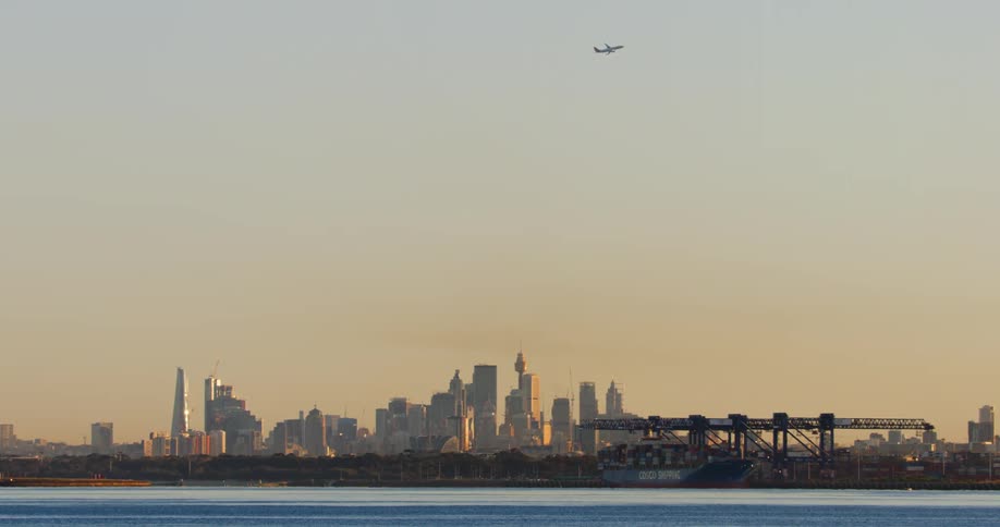 View of a metropolitan city by the sea with a cargo ship and in the sky an airplane taking off