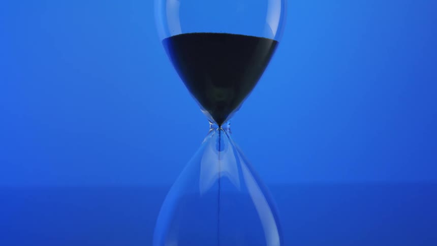 Black sand falls through center of hourglass against an electric blue background