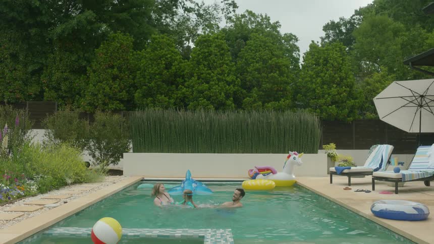 Father mother and daughter in a swimming pool playing pool ball at midday