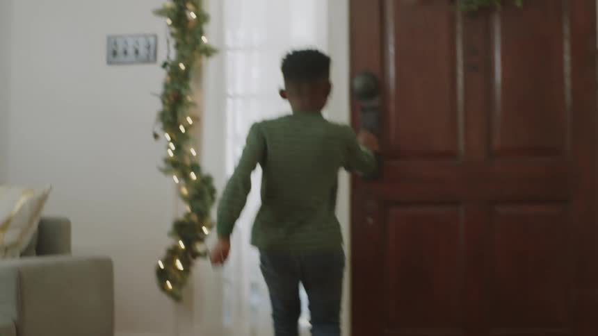 A young boy wearing boots excitedly runs to open the door