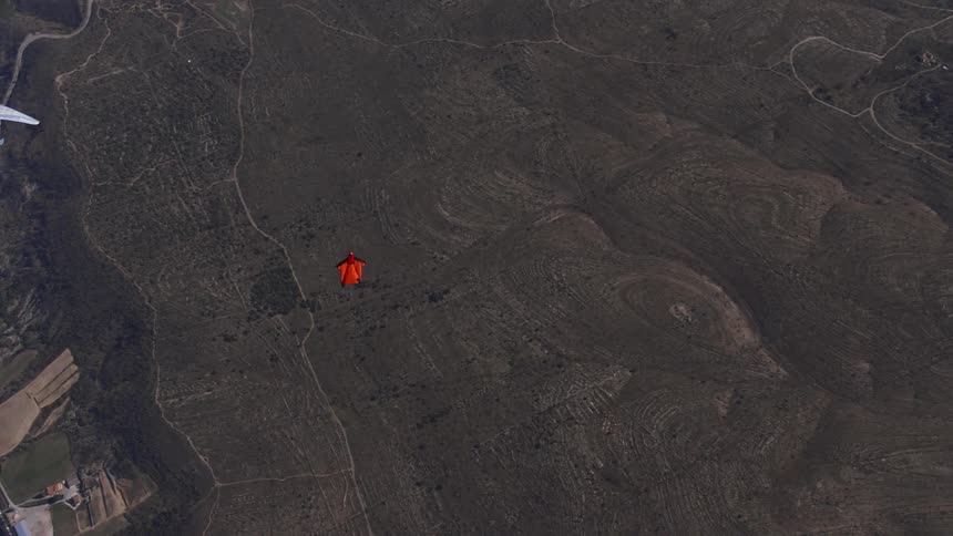 An aerial view of person skydiving and moving from a vegetation area to a small town close by
