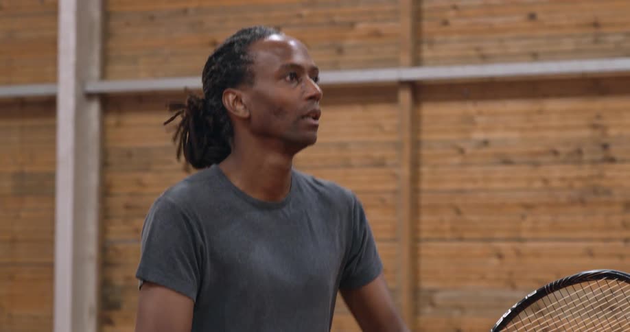 A black man with a tennis racket hits the ball