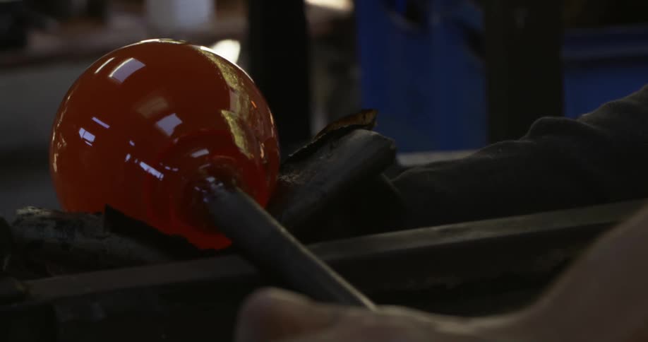 A person shapes red glass at work