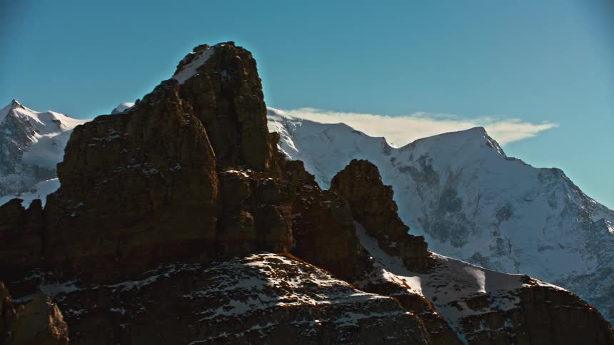 The sun shines upon snow covered mountains and rough peaks under a blue sky