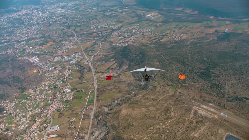 One person gliding in a hang glider and two others in wing suits