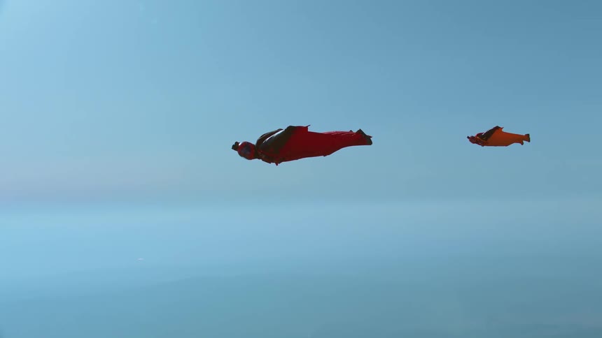 Two people flying with red wingsuits on the blue sky