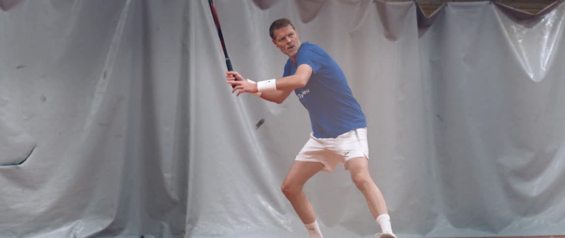 An adult man is jumping and preparing to hit a ball with a tennis racket