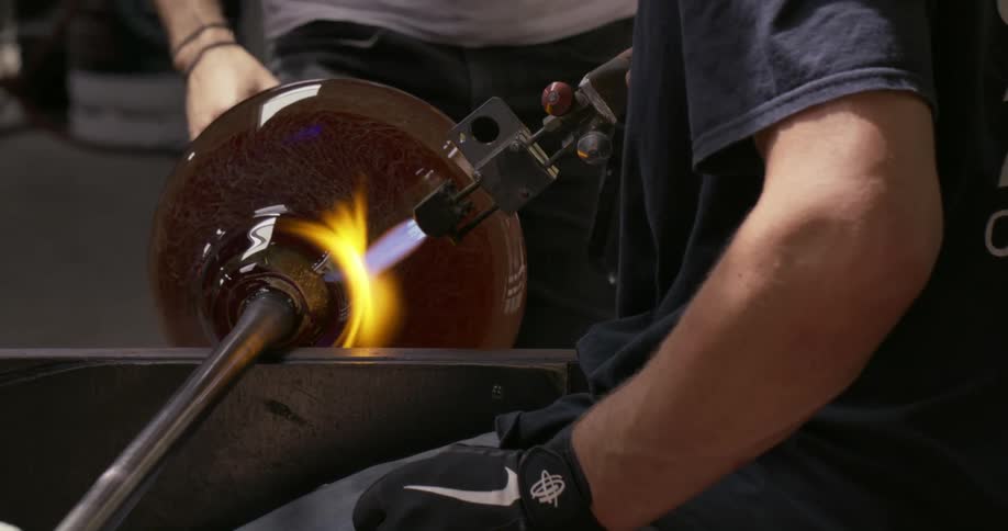 Artisan turning and heating a glass vase under a torch