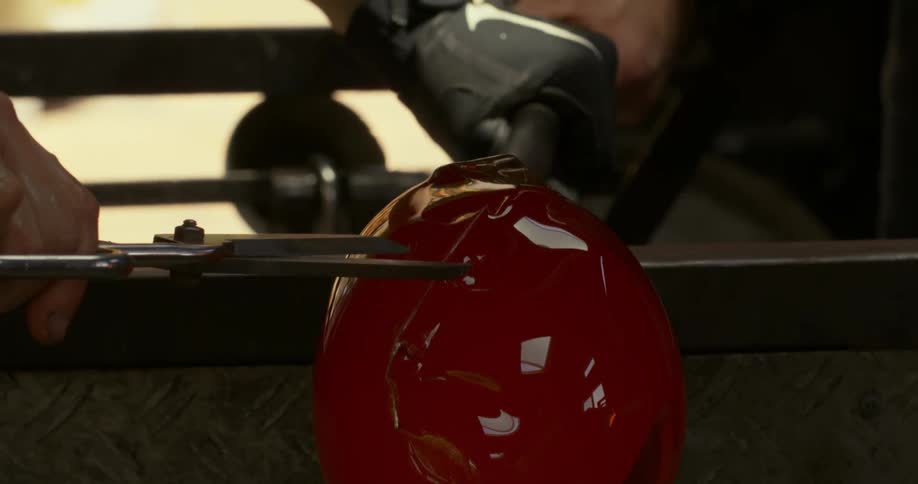 A person wearing gloves is cutting glass that is melted with heat