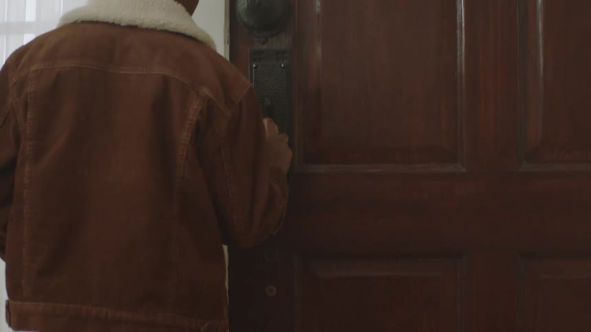 A young boy runs to the door and stares at the handle