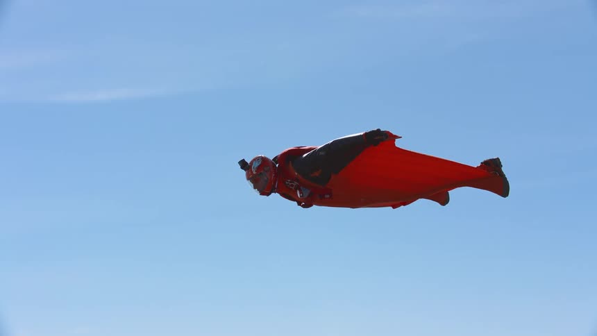 A skydiver wearing a wingsuit flies across the blue sky