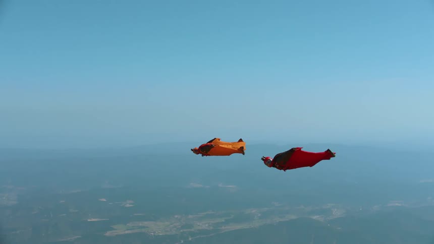 Two people wearing wingsuits fly over the landscape