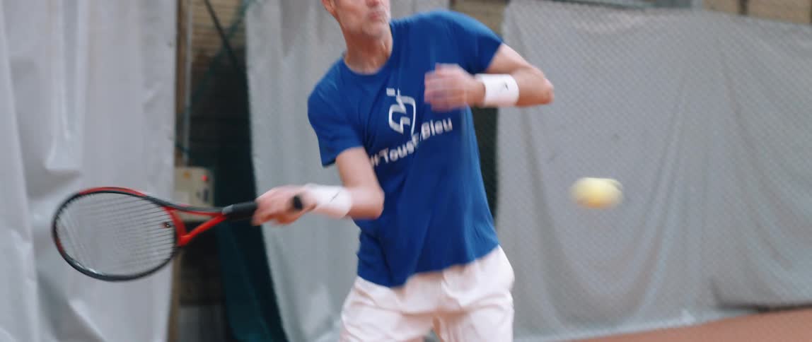 A middle aged man is playing tennis and hit the ball at a tennis court