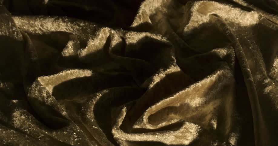 A gold velvet fabric is being displayed under different lighting from dark to bright and then dark again