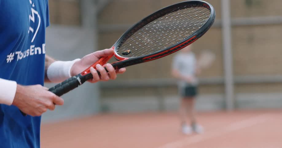A person in a blue tshirt is jumping and with a tennis racket in his hand