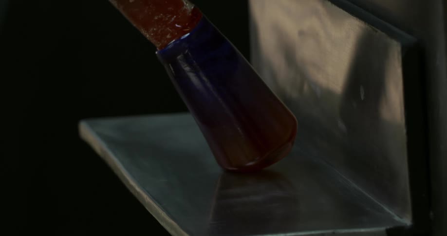 A piece of hot molten glassware takes shape over a metal shelf