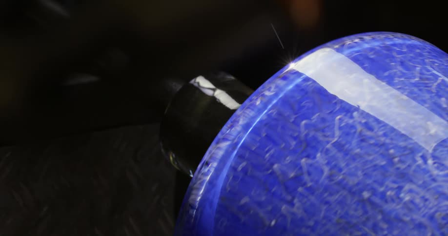 A blue glass rotates while a machine sands the bottom of it
