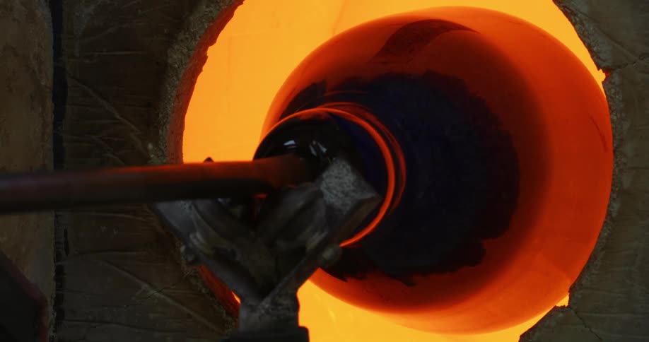 Molten glass at the tip of a pipe turning inside a hot oven
