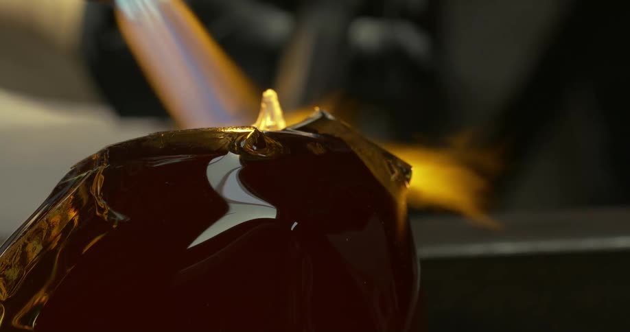 A large bulb of glass with folds and creases spins stopping half turn as it is heated with a torch flame