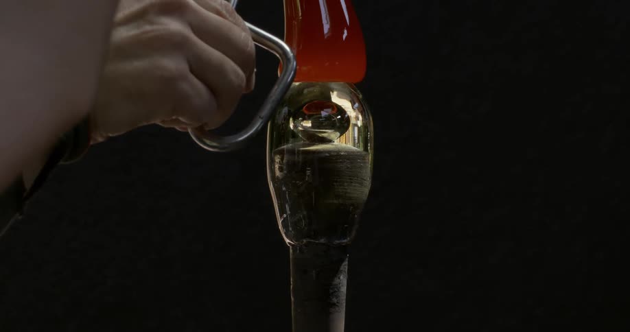 A persons hands placing superheated glass above a manufacturing stake