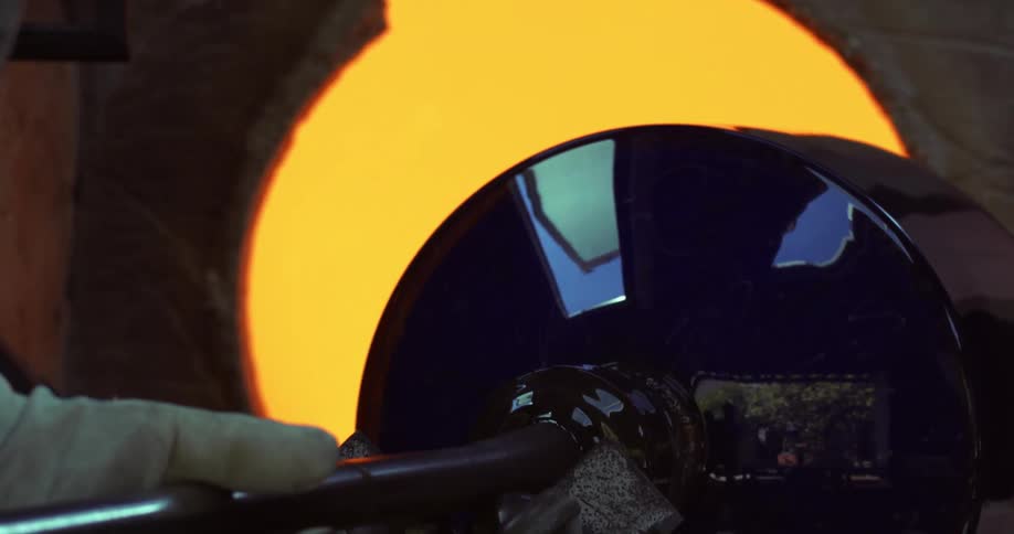 A person taking out a glass vase that is on a handle inside a hot forge