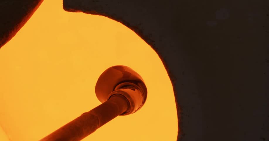 Molten glass at the tip of a pipe turning inside a hot oven