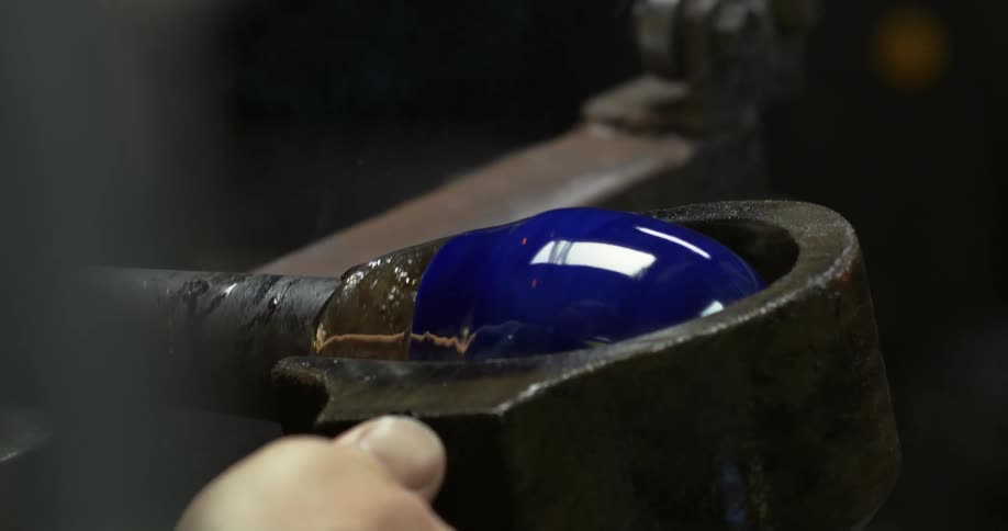 A blue glass vase being shaped by human hands