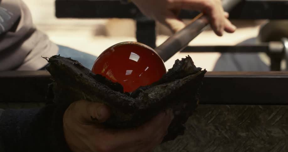 A man turns a rod with an orange glass sphere at the top