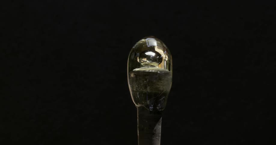 A glass orb piece of art on the tip of a glass molding pole being spun in front of a dark background with the room lights reflecting in it