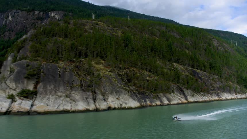 Person rides jet ski through water following base of slope