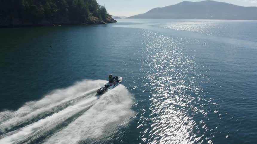 A woman rides a jet ski across a lake on a sunny day