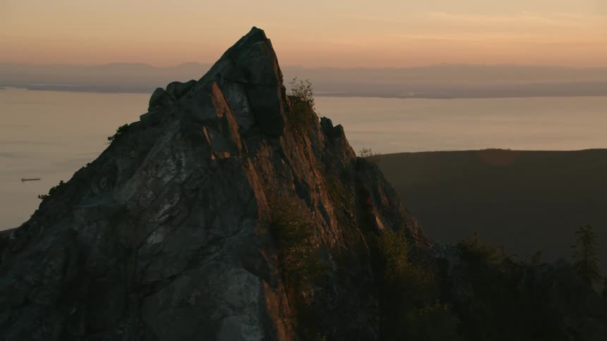 Aerial view of a towering mountain peak with a distant city skyline silhouetted at sunset