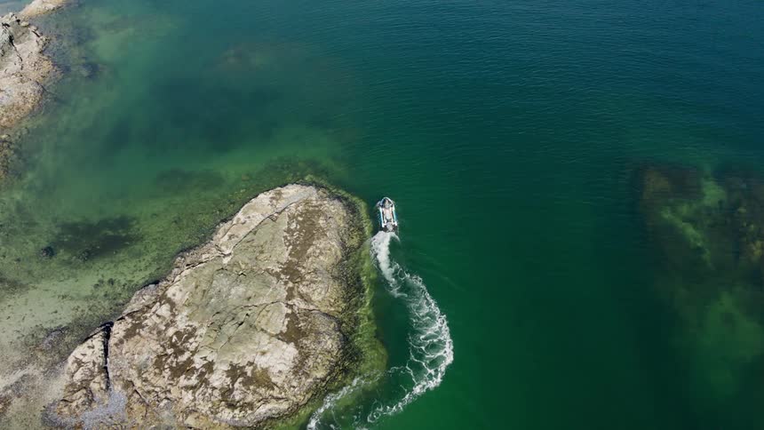 Aerial view of a jet ski navigating around a rock near the shoreline