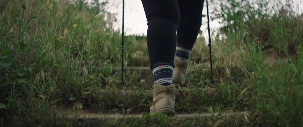 Woman with hiking poles black leggings and a pair of brown boots goes up outdoor stairs