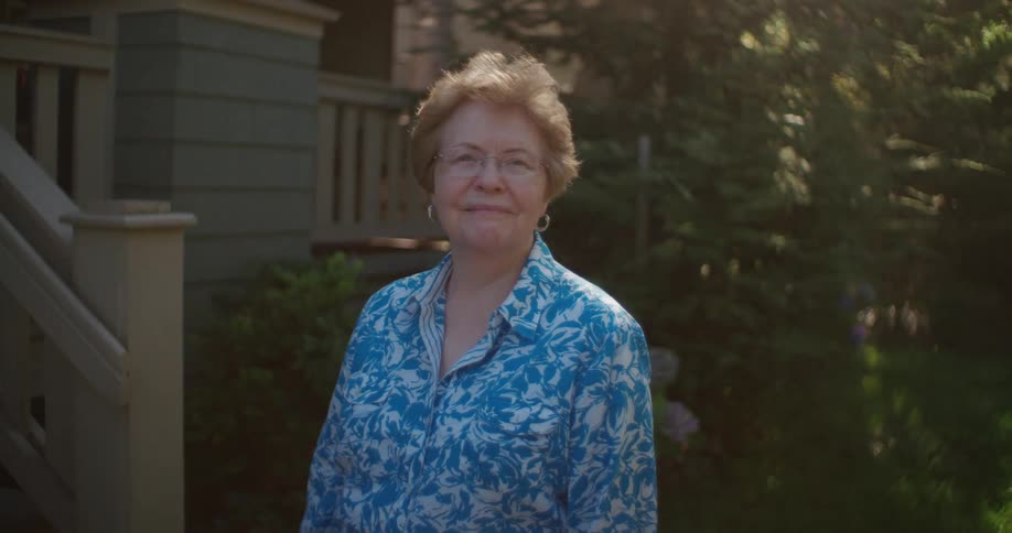 Woman with glasses and blue shirt smiles at camera in front of the porch