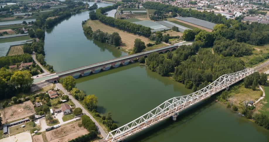 Bridges cross river near business complex and crop fields a short distance from a residential neighborhood