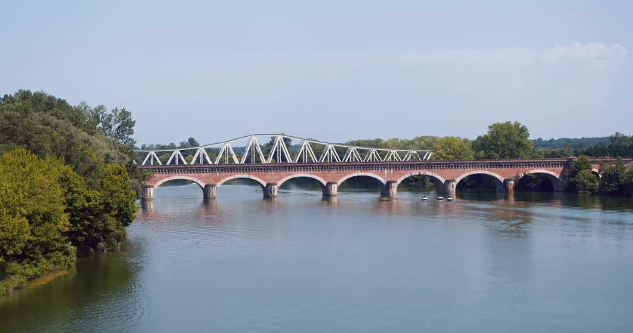 A red bridge crossing a huge river with vegetation on the sides