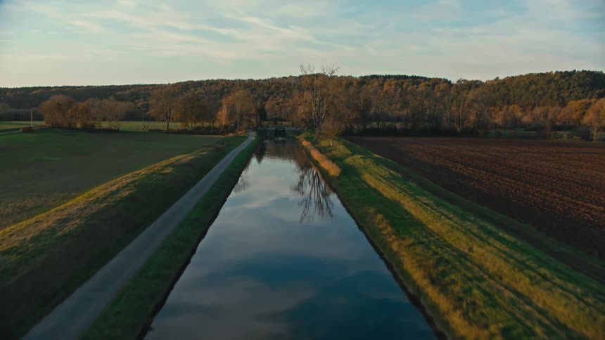 Lane parallels reflective river through fields and toward woods during fall on a cloudy day