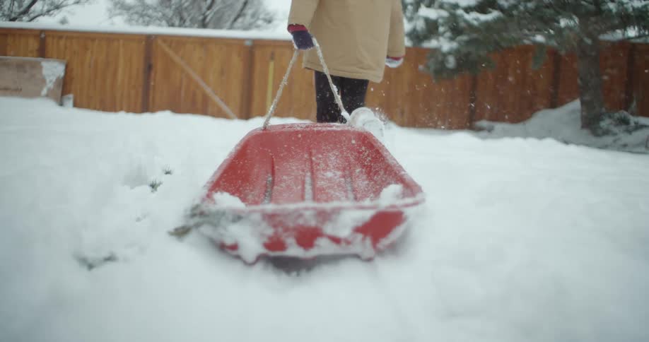 A little kid pulls a red sled on the snow in the backyard