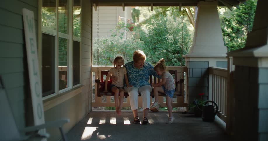 Girls run to their grandmother sitting on a chair in the porch