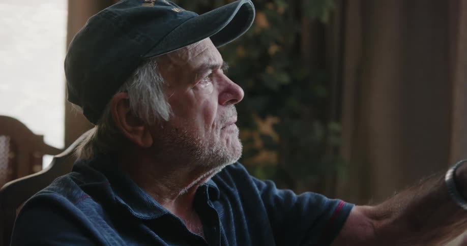 An elderly man deep in thought while sitting on a chair indoor