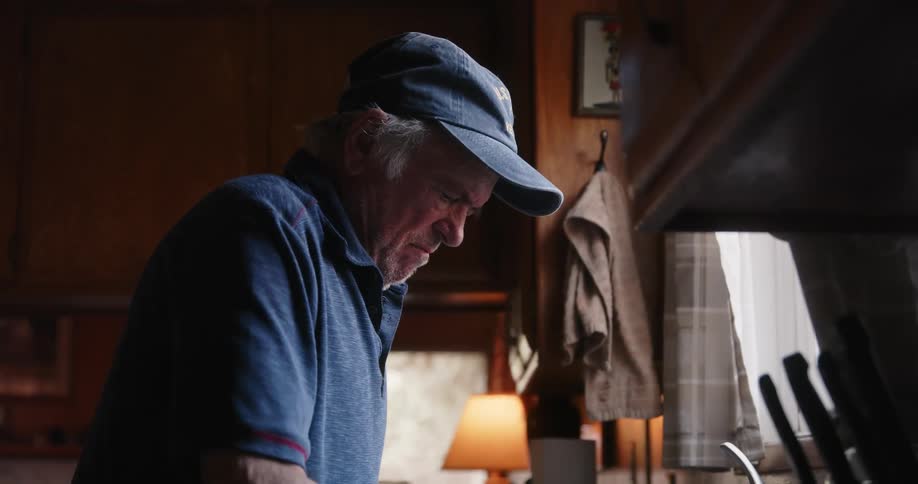 An elderly person in the kitchen cleaning at the sink